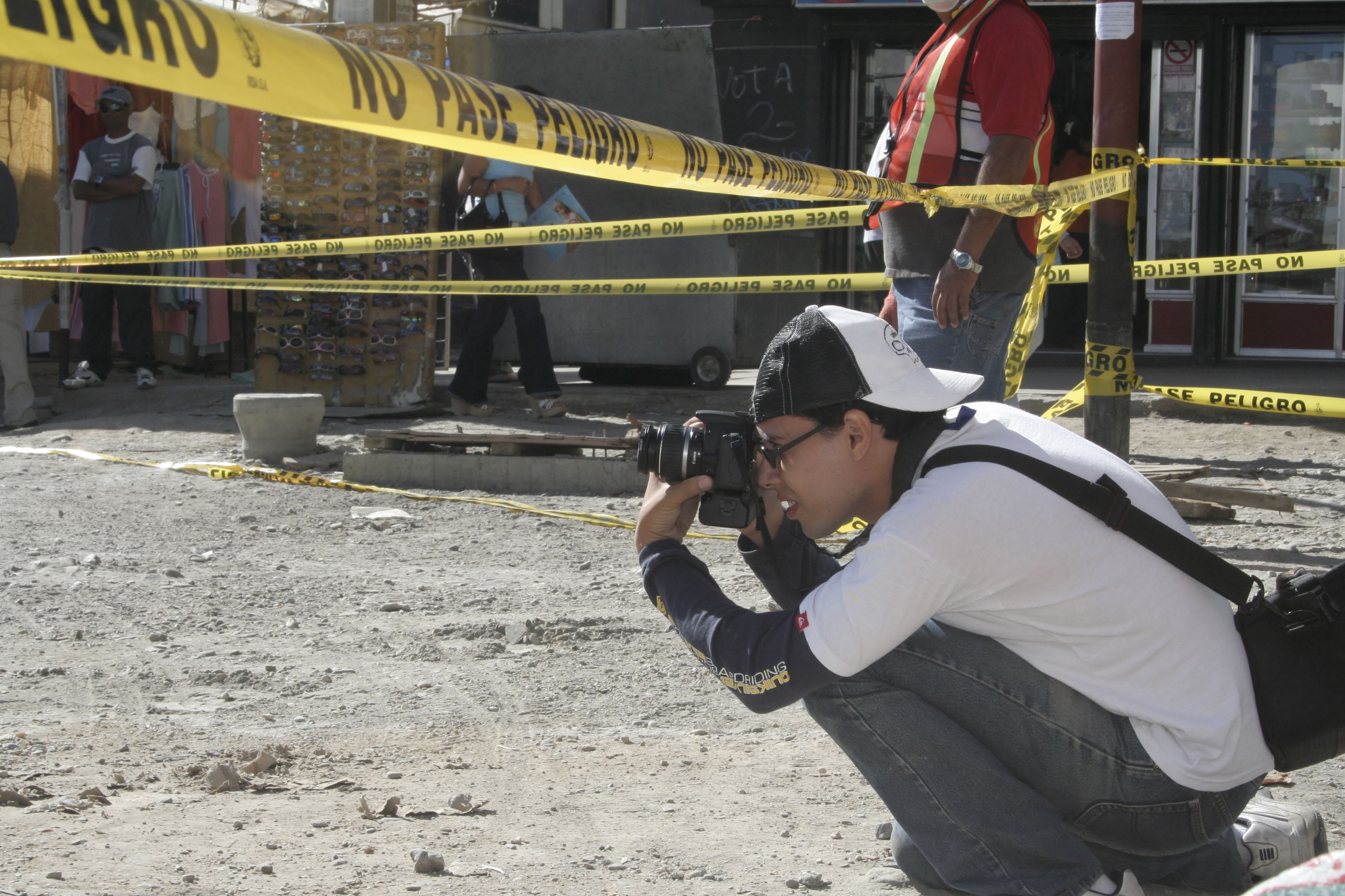 Gustavo López crouched behind police tape, photographing a street scene in Venezuela.